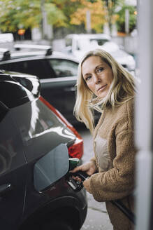 Reife Frau mit blondem Haar beim Tanken im Auto an der Tankstelle - MASF35155