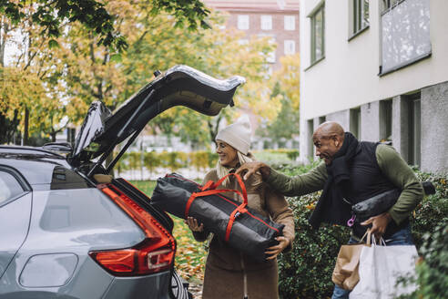 Man assisting woman loading luggage in car trunk while relocating house - MASF35169