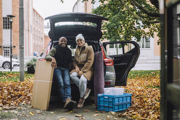 Porträt eines lächelnden reifen Paares mit Pappkarton und Kiste im Auto sitzend im Herbst - MASF35175
