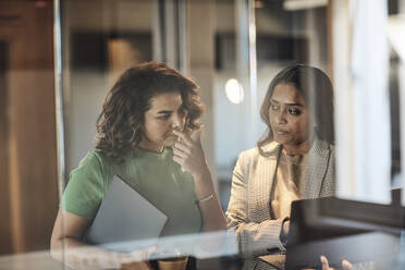 Businesswoman looking at laptop held by female colleague at office - MASF35244