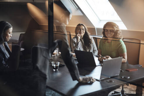 Female entrepreneurs discussing over laptop seen through glass during meeting in office - MASF35252