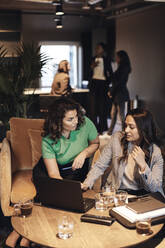Multirassische Geschäftsfrauen diskutieren über Laptop, während sie am Tisch im Büro sitzen - MASF35265