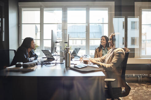 Multirassische Geschäftskolleginnen diskutieren am Schreibtisch sitzend im Büro die Strategie - MASF35276