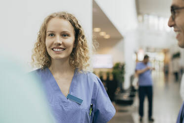 Lächelndes weibliches Gesundheitspersonal mit Kollegen im Krankenhaus - MASF35284