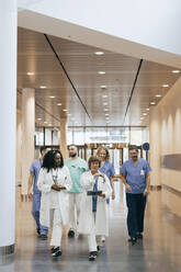 Male and female healthcare workers discussing while walking in hospital - MASF35288
