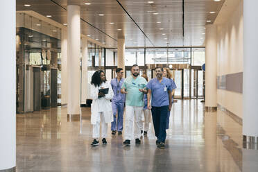 Multiracial group of male and female hospital staff discussing while walking in lobby - MASF35290