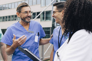 Happy male physician gesturing while talking with hospital staff - MASF35297