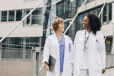 Glückliche weibliche Ärzte, die sich gegenseitig ansehen, während sie vor einem Krankenhaus stehen - MASF35304