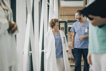 Mature male physician talking with female doctor while walking in corridor at hospital - MASF35336