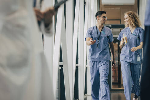 Smiling male and female healthcare staff walking in corridor of hospital - MASF35339