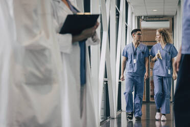 Krankenschwester mit Banane im Gespräch mit einem Kollegen auf dem Flur eines Krankenhauses - MASF35340