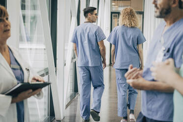 Rear view of male and female healthcare workers walking in corridor - MASF35341