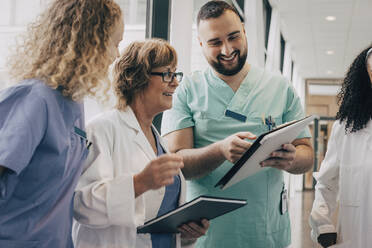 Lächelndes multirassisches Ärzteteam bespricht sich über einem Klemmbrett im Krankenhaus - MASF35345