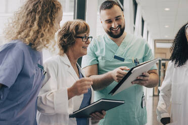 Smiling multiracial medical team discussing over clipboard at hospital - MASF35345