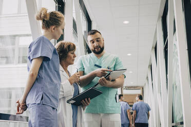 Male healthcare worker explaining over clipboard to doctor at hospital - MASF35347