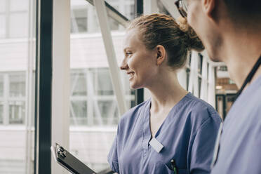 Smiling female nurse looking through window at hospital - MASF35348