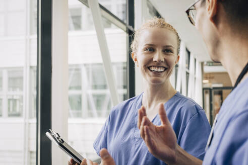 Glückliche junge Krankenschwester im Gespräch mit einem männlichen Kollegen im Krankenhaus - MASF35349