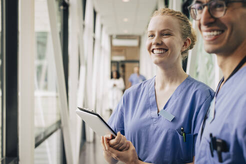 Glückliche Krankenschwester, die wegschaut und ein Klemmbrett im Krankenhaus hält - MASF35350