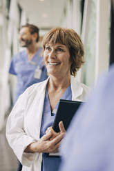 Happy female doctor looking away while standing in hospital - MASF35354