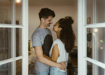 Side view of smiling couple looking at each other seen through doorway - MASF35392