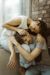 Smiling man with eyes closed resting on girlfriend's lap while sitting at home - MASF35399