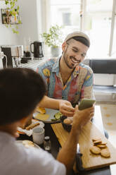 Mann teilt Smartphone mit Freund beim Essen zu Hause - MASF35416