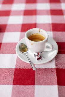 Empty coffee cup lying on red checked tablecloth - KSWF02278