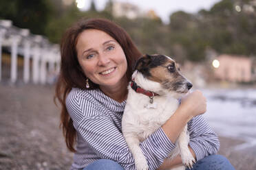 Happy woman holding dog at beach - NJAF00242