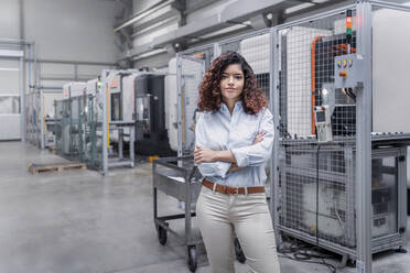 Smiling engineer with arms crossed standing in front of machine - AAZF00031