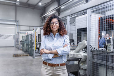 Glücklicher Ingenieur mit verschränkten Armen in der Industrie stehend - AAZF00032