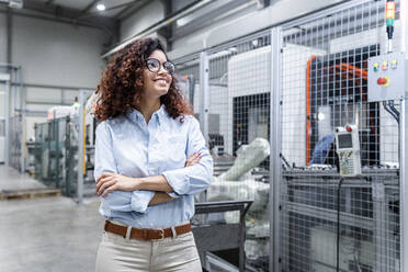 Happy young engineer with arms crossed standing in factory - AAZF00033