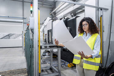 Engineer examining blueprints standing by machine in industry - AAZF00041