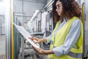 Young engineer examining blueprints in industry - AAZF00042