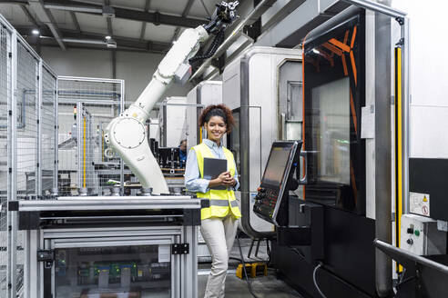 Smiling engineer standing with tablet computer by machine in factory - AAZF00049