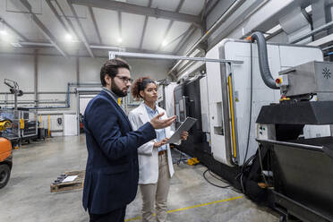 Engineers discussing over machine in factory - AAZF00076