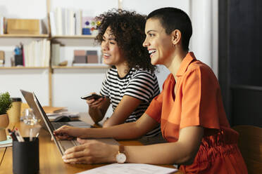 Zufriedene Geschäftskollegen, die am Tisch vor ihren Laptops sitzen - EBSF02729