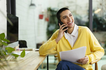 Happy freelancer talking through mobile phone at table - EBSF02762