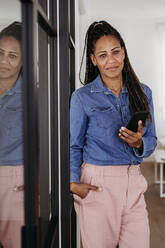 Lächelnde Frau stehend mit Smartphone zu Hause - EBBF07922
