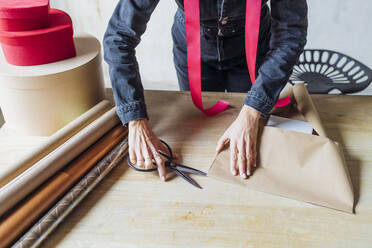 Woman cutting wrapping paper with scissors on desk - MEUF08871