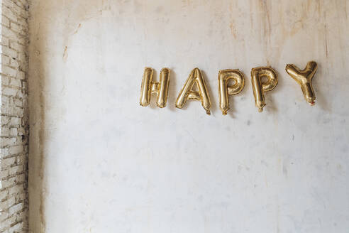 Gold colored happy text made with inflated balloons hanging on wall - MEUF08889