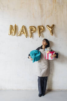 Happy woman with gift boxes leaning on wall - MEUF08890