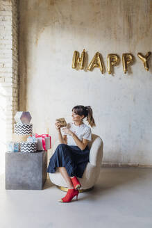 Happy woman sitting with gift boxes on chair - MEUF08896