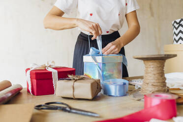 Frau bindet Schleife an Geschenkbox am Schreibtisch - MEUF08905