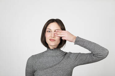 Young woman covering eye against white background - LMCF00027