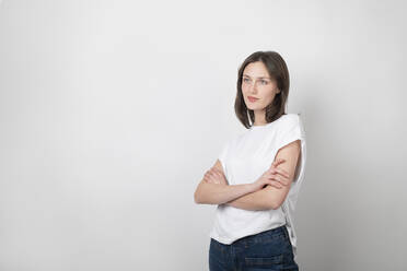 Contemplative woman standing with arms crossed against white background - LMCF00033