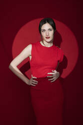 Confident beautiful woman with hands on hips against red background - LMCF00056