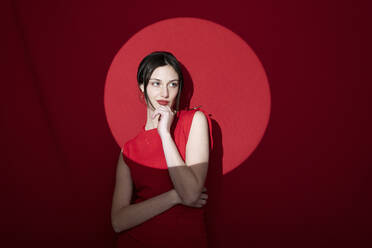 Thoughtful young woman standing with hand on chin over colored background - LMCF00058