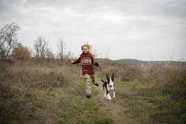 Smiling girl running with dog through grass - ALKF00091