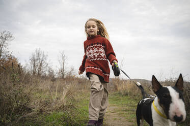 Girl running with Bull Terrier amidst grass - ALKF00093