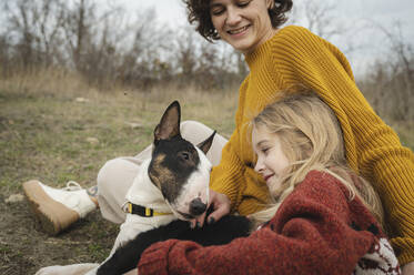 Happy mother and girl sitting with Bull Terrier dog - ALKF00107